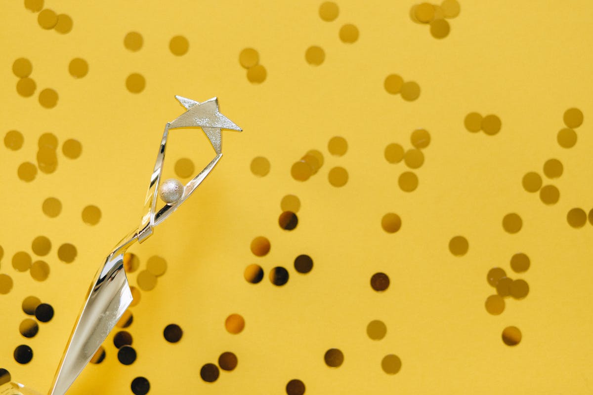 A silver trophy with a star design on a vibrant yellow background adorned with confetti.